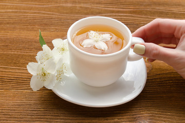 Female hand and a white mug of tea with jasmine on a wooden table. Close-up