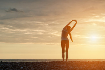 Girl doing morning exercises at the beach. Dawn. View from the back