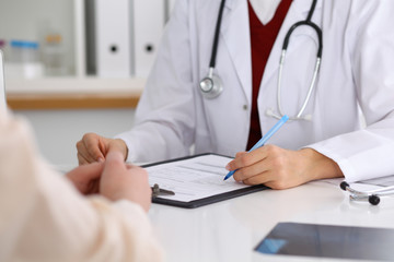 Close up of a female doctor filling up  an application form while consulting patient