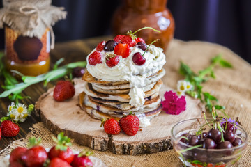 Delicious pancakes with berries on the authentic wooden stand. Summer food, pancakes sprinkled with cream and berries