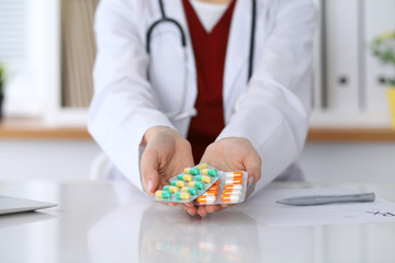 Female doctor hand holding pack of different tablet blisters at workplace closeup