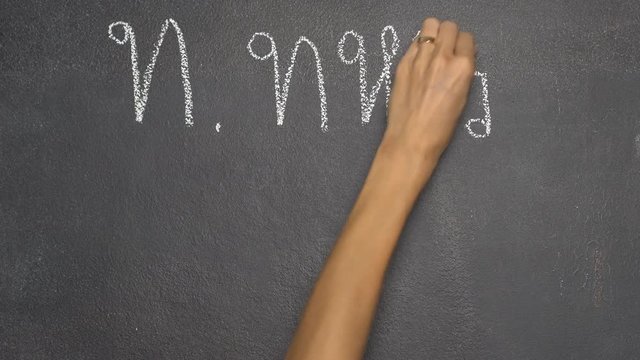 Woman's hand writing Thai letter "ท" with white chalk on blackboard