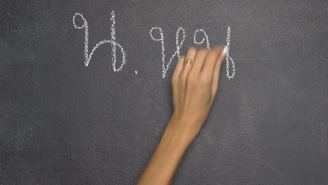 Woman's hand writing Thai letter "น" with white chalk on blackboard