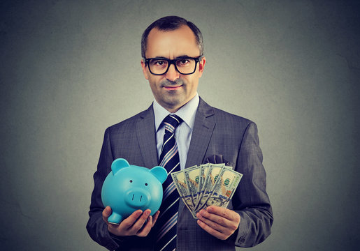 Serious business man in glasses with piggy bank and dollar cash banknotes