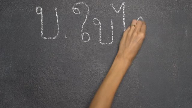 Woman's hand writing Thai letter "บ" with white chalk on blackboard