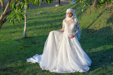 Fototapeta premium Portrait of a beautiful muslim bride with make up in white wedding dress with beautiful white headdress natural light.
