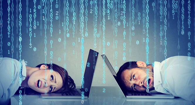Stressed business woman and man resting head on laptop under binary code rain sitting at table