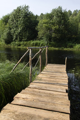 Obraz premium wooden bridge from boards with handrail Summer day on forest river in north of Russia