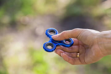 Spinner in girls hand close-up. Hand holds blue fidget closeup.
