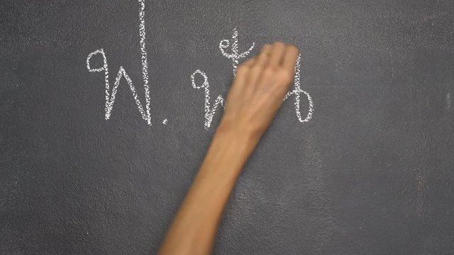 Woman's hand writing Thai letter "ฟ" with white chalk on blackboard