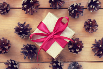 Christmas surprise/ gift wrapped in craft paper tied with a red bow against the background of fir cones