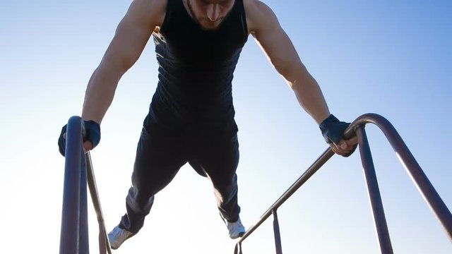 Strong man making triceps fall on parallel bars in the park.
