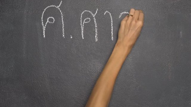 Woman's hand writing Thai letter "ศ" with white chalk on blackboard