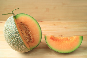 Fresh ripe muskmelon sliced from the whole fruit isolated on a wooden table 