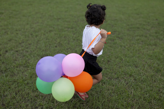 A kid playing with balloon in a greenfield