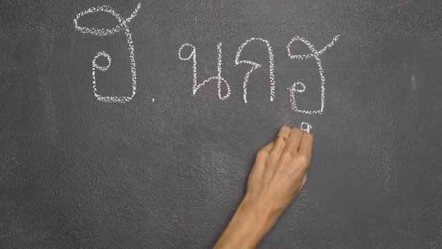 Woman's hand writing Thai letter "ฮ" with white chalk on blackboard