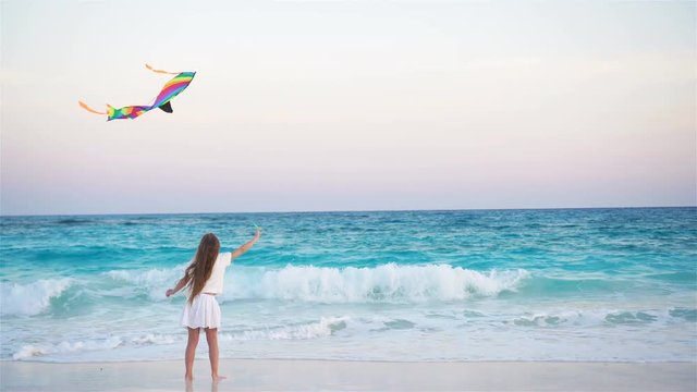 Little girl with flying kite on tropical beach at sunset. Kid play on ocean shore. Child with beach toys.
