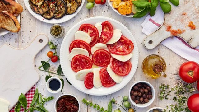 Making of Caprese salad with sliced fresh tomatoes, mozzarella cheese and basil served on a white plate on a wooden table, top view. Traditional Italian food. Stop motion animation