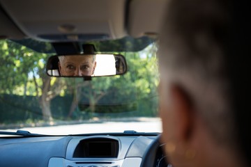 Senior woman looking into rear view mirror while driving a car