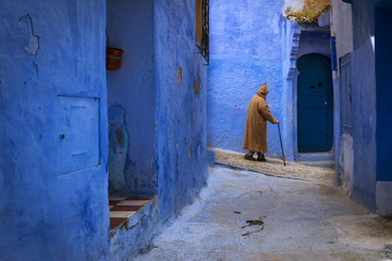 Obraz na płótnie Canvas Chefchaouen, Morocco - April 10, 2016: Moroccan man walking in a narrow street in the town of Chefchaouen in Morocco, North Africa