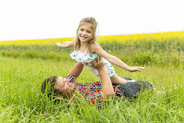 Fototapeta premium Happy family father and child daughter on yellow flowers on nature in summer