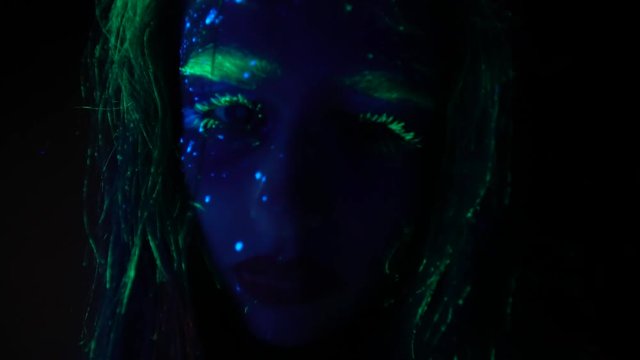 The camera on the girl's hands approaches the face painted with fluorescent paint