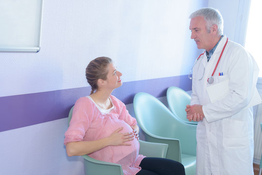 smiling pregnant woman talking with doctor in hospital corridor