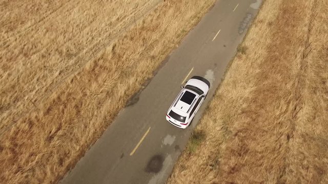 Aerial footage of white 4x4 SUV car driving on the deserted highway between dry grass