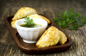 Empanadas with chimichurri sauce on wooden table