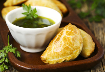Empanadas with chimichurri sauce on wooden table
