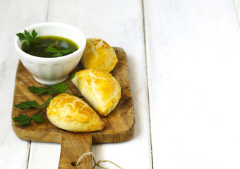 Empanadas with chimichurri sauce on wooden table