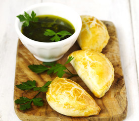 Empanadas with chimichurri sauce on wooden table