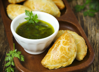 Empanadas with chimichurri sauce on wooden table