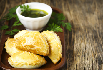 Empanadas with chimichurri sauce on wooden table