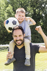 Young father with his little son playing football on football pitch