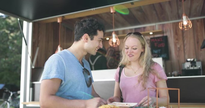 Young adult couple eating outside at food truck at music festival