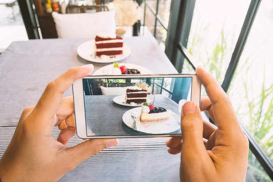 Hand holding smartphone and taking photo of delicious cake