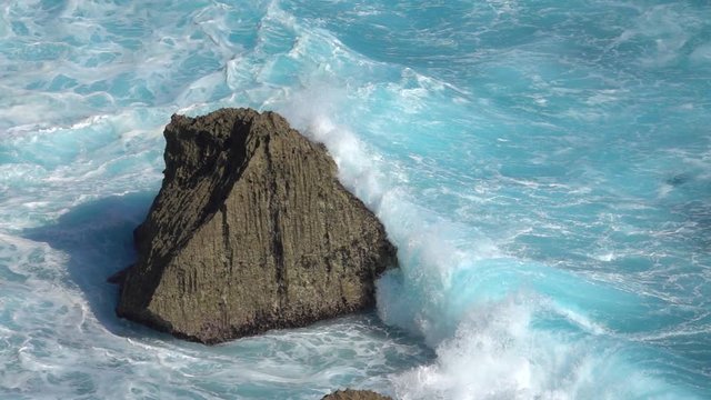 SLOW MOTION CLOSE UP: Turbulent foamy ocean waves breaking over sharp rocky reef. Raging barrel wave hitting the shore splashing over shoal. Powerful surf break crashing into rock spraying water drops