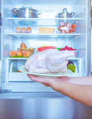 Open refrigerator filled with food. Hands holding a chicken © freepeoplea