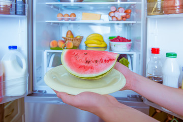 Open refrigerator filled with food. Hands holding watermelon © freepeoplea