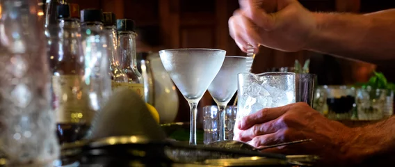 Raamstickers Cocktail Barman roert een cocktail met bewegingsonscherpte. Selectieve focus op de ijzige glazen. Uitzicht van achter de bar.