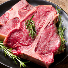 Raw meat t-bone steak and seasoning on wooden background