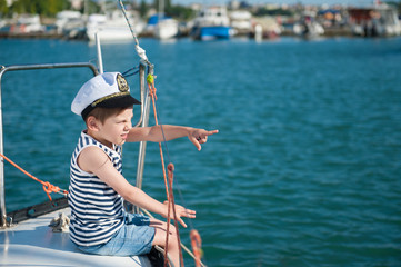 handsome little captain boy pointing with his finger to the distance sitting on luxury yacht in...
