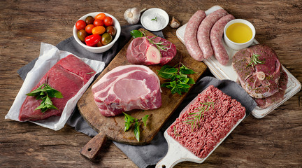 Different types of fresh raw meat on a rustic wooden background.