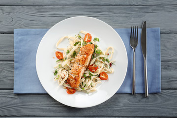 Plate with tasty salmon and pasta on wooden table