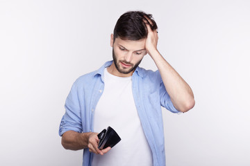 Studio shot isolated on white wall. Young bearded man dressed casual  found his  stylish black leather wallet almost empty. The crisis hits financial well-being of handsome Caucasian office manager.