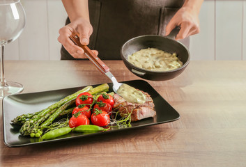 Man adding sauce to sliced steak with vegetables on plate