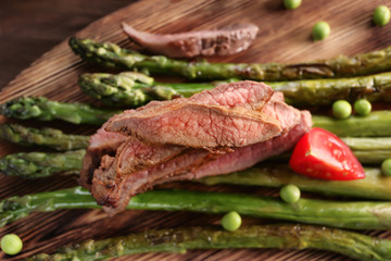 Sliced steak served with asparagus on wooden board
