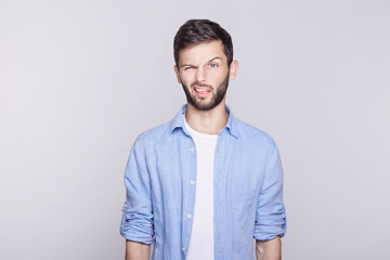 Fototapeta premium Emotional and stylish young Caucasian blue eyed handsome man employee wearing blue jacket on white t-shirt grimacing, making mouths at camera trying to tease someone, acting like little naughty child.