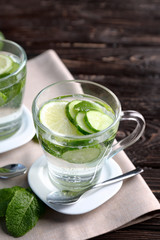 Delicious refreshing water with mint and cucumber in cup on wooden table